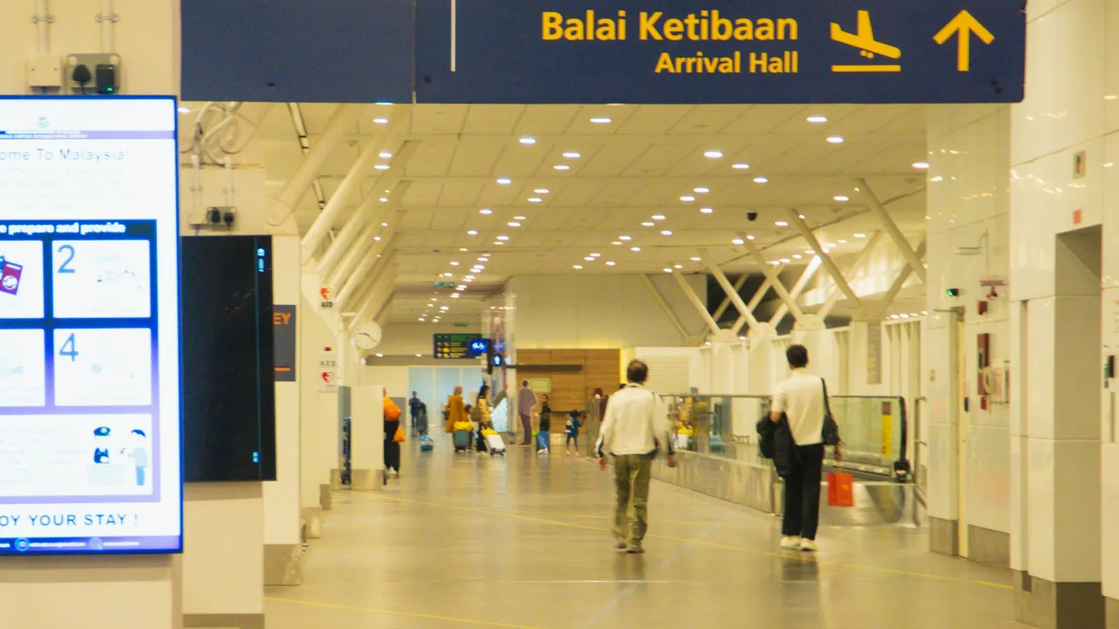 Travelers walking beneath an Arrival Hall sign in a Malaysian airport terminal