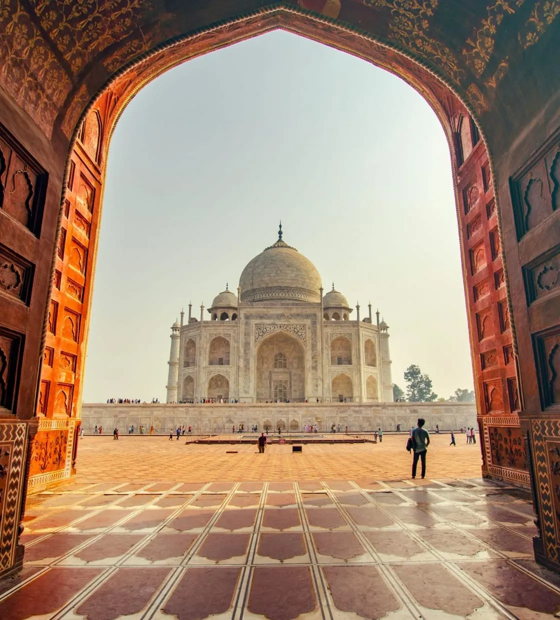 The Taj Mahal seen through a carved sandstone archway, with a traveler in the courtyard